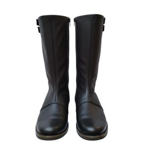 May include: A pair of black leather knee-high boots. The boots have a smooth texture, a zipper on the side, and a buckle detail near the top. The soles are a contrasting brown color.