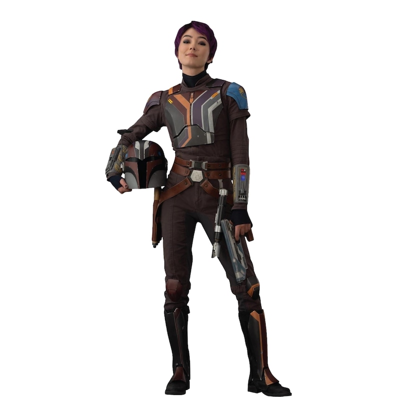 May include: A person in a brown and gray costume with a helmet, holding a blaster. The costume has a chest plate with orange, gray, and purple accents. The person is wearing black boots and a utility belt. The helmet is brown and gray.