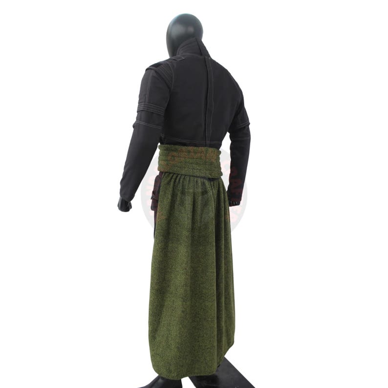 May include: A black outfit with a long green skirt and a wide green belt. The top is a black jacket with long sleeves. The outfit is displayed on a mannequin.