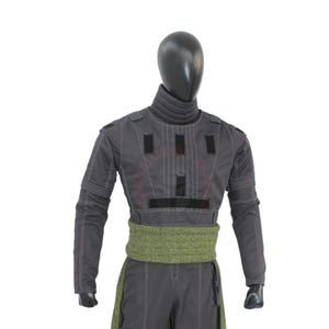 May include: A gray costume with a high collar and long sleeves, featuring black rectangular accents and white stitching. A green patterned sash wraps around the waist. The costume is displayed on a black mannequin.