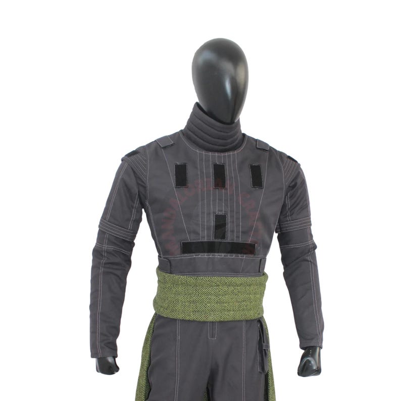 May include: A gray costume with a high collar and long sleeves, featuring black rectangular accents and white stitching. A green patterned sash wraps around the waist. The costume is displayed on a black mannequin.