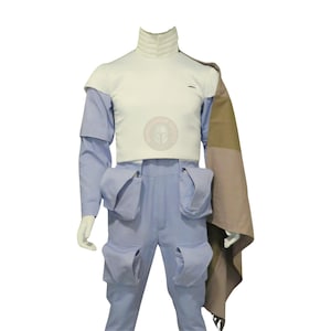 May include: A light blue costume with a white top and matching trousers. The costume features a high collar, shoulder pads, and multiple pockets. A brown and tan cape is draped over the shoulder. The costume is displayed on a mannequin.