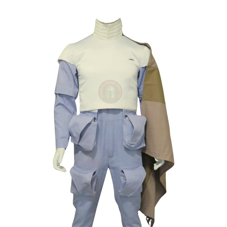 May include: A light blue costume with a white top and matching trousers. The costume features a high collar, shoulder pads, and multiple pockets. A brown and tan cape is draped over the shoulder. The costume is displayed on a mannequin.