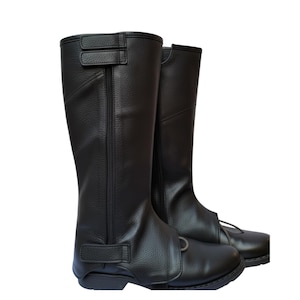 May include: A pair of black leather riding boots. The boots are knee-high with a textured finish and feature a zipper and adjustable straps. The boots have a classic design, suitable for equestrian activities.