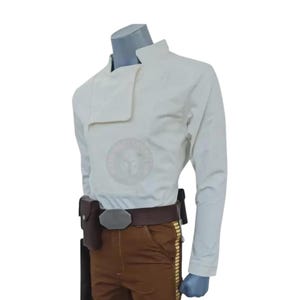 Può includere: Giacca color crema con un insolito colletto asimmetrico, abbinata a pantaloni marroni e una cintura marrone. La cintura ha una fibbia argentata e una fondina. L'outfit è esposto su un manichino.