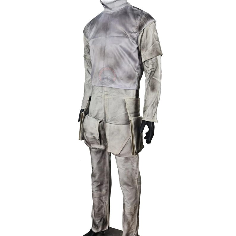 May include: A light grey costume with a high collar, long sleeves, and matching pants. The outfit features multiple pockets and a weathered appearance, suggesting a utilitarian or futuristic design. Black gloves complete the ensemble.