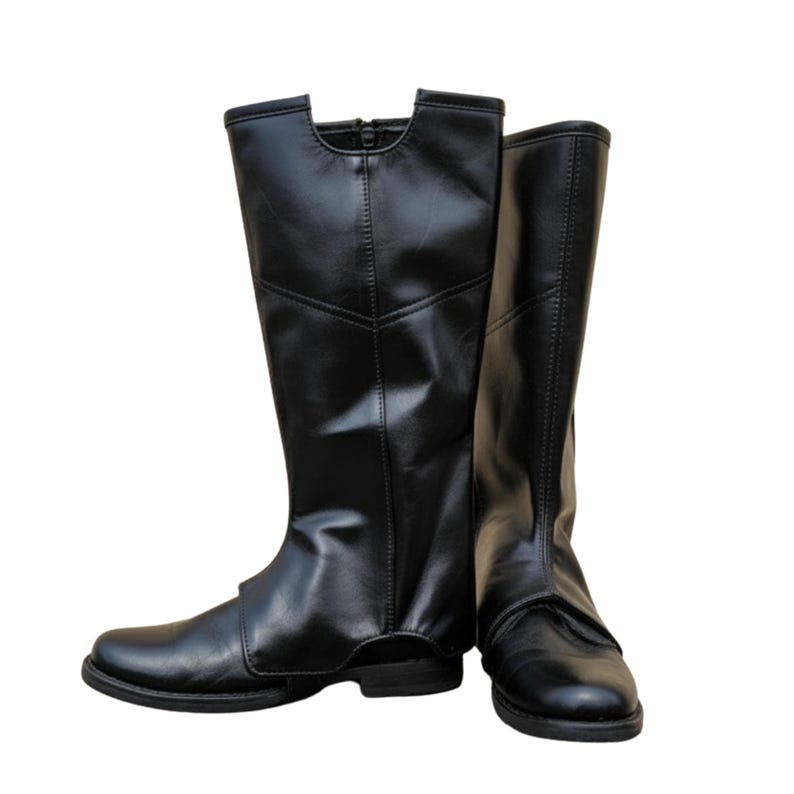 May include: A pair of black leather knee-high boots. The boots have a smooth, shiny finish and a rounded toe. The top of the boots have a unique cut-out design. The boots are standing upright against a white background.