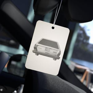 Puede incluir: Un ambientador rectangular con una ilustración de coche y el texto "DILLY DALLY". El ambientador está colgado de un hilo, con un interior de coche en el fondo.