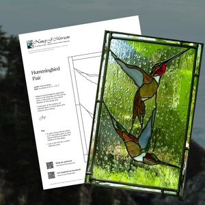 May include: A stained glass panel featuring two hummingbirds in flight, with a green and yellow background. The panel is framed in a dark metal. A white paper with the text "Hummingbird Pair" is in the background.
