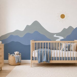 Könnte beinhalten: Ein Wandbild mit einer geschichteten Berglandschaft in Blau- und Grautönen, einem geschwungenen weißen Flusslauf und einer goldenen Sonnengrafik. Das Design ist auf einer glatten Wand hinter einem hölzernen Kinderbett angebracht.