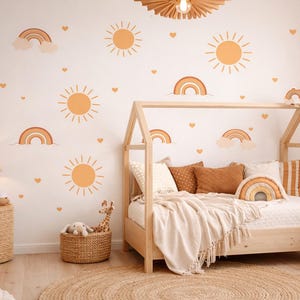 May include: A child's bedroom with a wooden house-shaped bed, decorated with sun, rainbow, and heart wall decals. The room features a woven side table with a lamp, a round jute rug, and a woven basket with stuffed animals. The color scheme is warm and inviting.