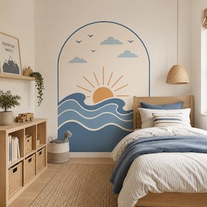 May include: A wall decal featuring an arched design with a stylised orange sun rising over blue ocean waves, accompanied by light blue clouds and small birds in flight. The graphic is applied to a neutral wall above a wooden bed frame.