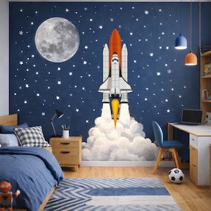May include: A bedroom decorated with a space theme. A large rocket ship mural is on the dark blue wall, with a moon and stars. The room has a bed, desk, chair, and a football on the floor. The rocket ship is white, orange, and yellow.