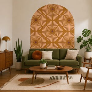 Pode incluir: Um adesivo de parede em forma de arco com um padrão repetitivo de flores grandes e estilizadas em tons de rosa claro e laranja escuro. O design é aplicado numa parede lisa acima de um sofá verde, criando um ponto focal geométrico.