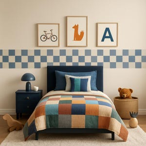 Op de afbeelding: Een kinderkamer met een marineblauw bed, een patchwork quilt en ingelijste kunst. De kunst omvat een fiets, een vos en de letter "A". Een blauw nachtkastje met een lamp en een teddybeer in een mand maken de scène compleet.