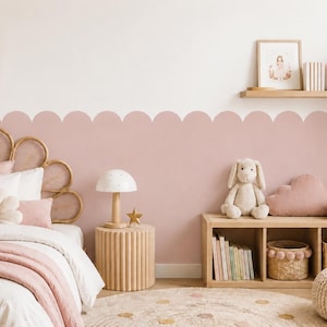 May include: A bedroom featuring a scalloped pink wall decal, a rattan headboard, a bed with pink and white bedding, a fluted wooden nightstand with a mushroom lamp, a wooden storage unit with books and baskets, and a plush rabbit toy.
