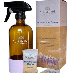 May include: Amber glass spray bottle with a black sprayer, a light purple base, and a cardboard box. The box and bottle feature the text "SUNSHINE SUSTAINABLES Multi-Purpose Cleaner Lavender". Two small packets of cleaner are also included.