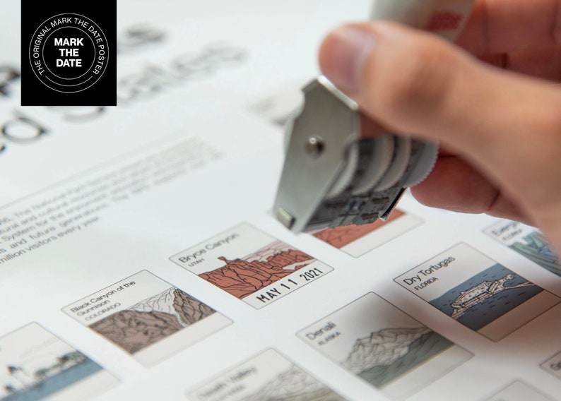 Op de afbeelding: Een witte en grijze stempel met een zwart inktkussen wordt gebruikt om een datum op een poster met een lijst van nationale parken te markeren. De datum is 11 mei 2021. De poster bevat illustraties van nationale parken, waaronder Bryce Canyon, Dry Tortugas en Black Canyon of the Gunnison.