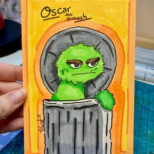 May include: Hand-painted artwork of Oscar the Grouch from Sesame Street. The illustration features Oscar in his trash can, set against a yellow and orange background. The text "Oscar the Grouch" is written above the character.