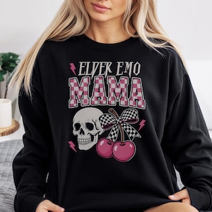 Può includere: Felpa nera con la scritta "ELVER EMO MAMA" in lettere rosa e a scacchi bianchi. Il design include un teschio, ciliegie rosa, un fiocco a scacchi e fulmini rosa. Uno stile casual e audace.
