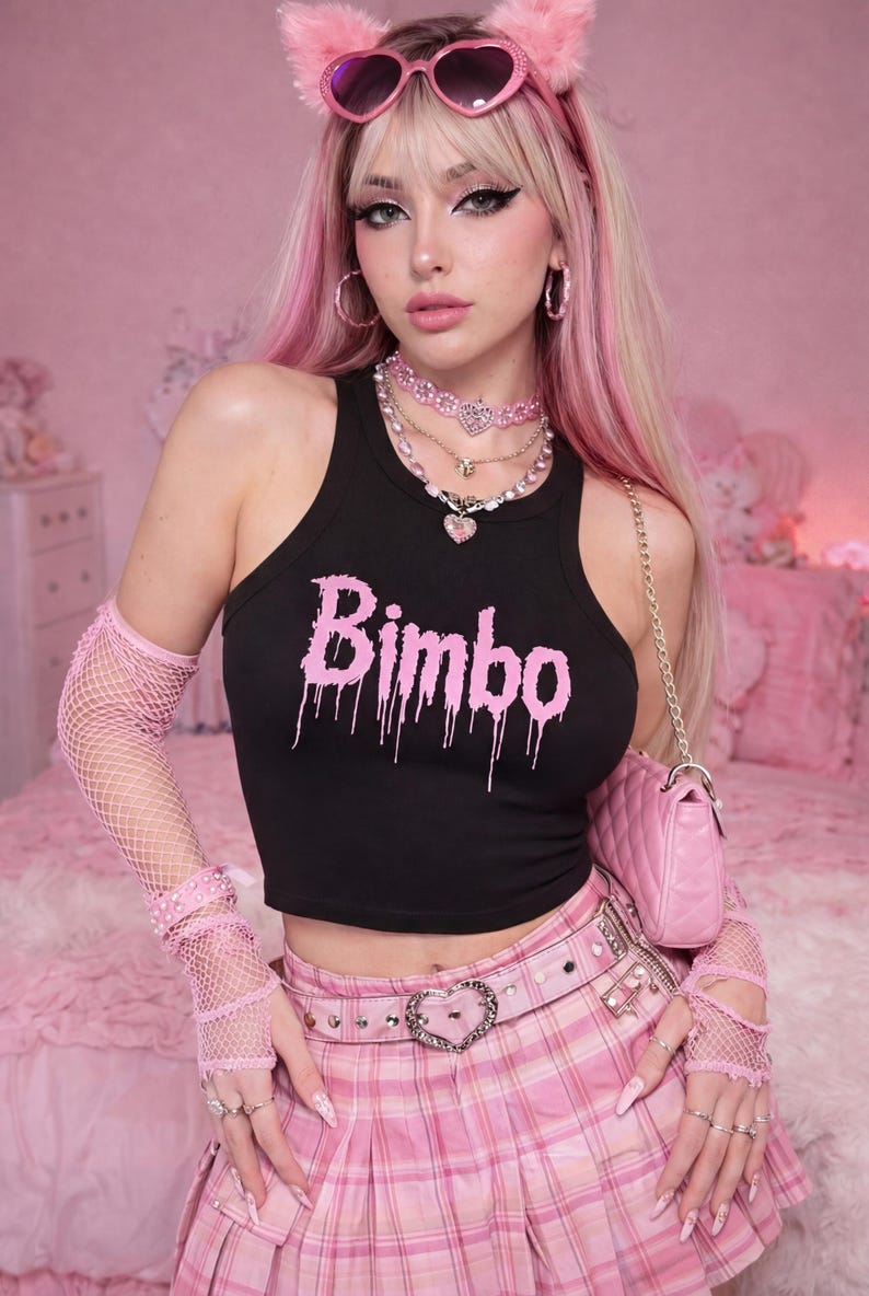 May include: Black crop top with the word "Bimbo" in pink dripping font. The model is wearing a pink plaid skirt, pink accessories, and a pink purse. The background is pink.
