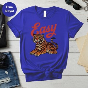 May include: Royal blue t-shirt with a tiger illustration in orange and black stripes, and the word "Easy" in red script. The tiger is lying down with its mouth open. The shirt is knotted at the waist.