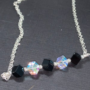 Puede incluir: Un collar de cadena de plata con cuentas de forma cúbica negras e iridiscentes.