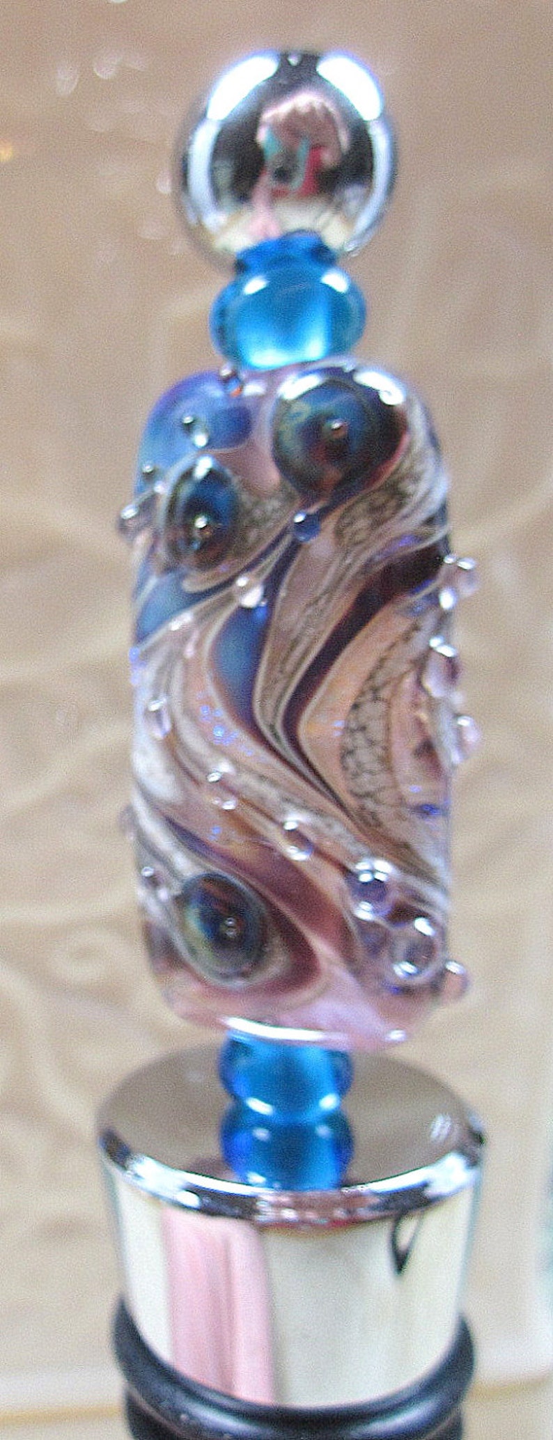 Peut inclure: Un bouchon de bouteille bleu et argent avec un motif tourbillonnant et une sph&egrave;re de verre transparente sur le dessus.