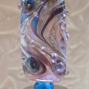Peut inclure: Un bouchon de bouteille en verre avec un dessus argent&eacute; et une perle en verre bleu et violet avec un motif tourbillonnant. La perle contient de petites bulles d'air.