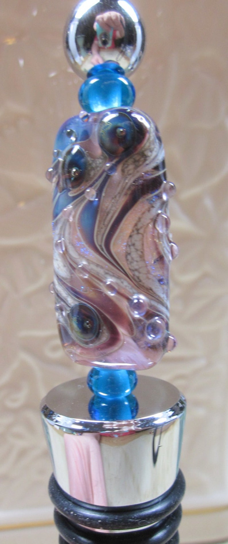Peut inclure: Un bouchon de bouteille en verre avec un dessus argent&eacute; et une perle en verre bleu et violet avec un motif tourbillonnant. La perle contient de petites bulles d'air.