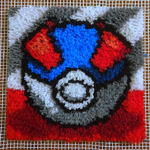 May include: A square, handmade rug with a colorful design. The rug features a central blue shape surrounded by red, gray, and white elements. The design is set against a white mesh background, creating a textured, artistic piece.