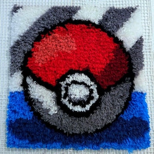 May include: A handmade, square rug featuring a vibrant Poké Ball design. The rug showcases a red and white sphere with a black outline and a central white button. The background includes blue, gray, and white sections.