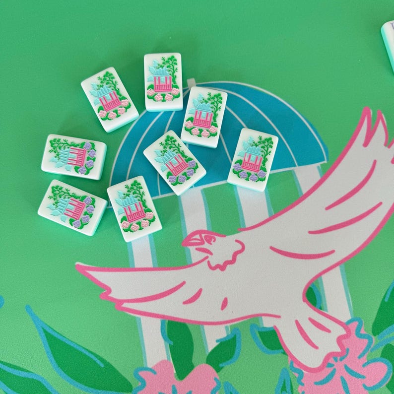 May include: A collection of white rectangular tiles with a pink and blue pagoda design, surrounded by green foliage. The tiles are scattered on a green surface with a white and pink bird illustration and a blue umbrella design.