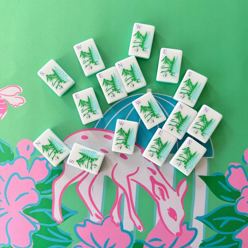 May include: A collection of white Mahjong tiles with green tree and directional symbols, including N, S, E, and W, scattered on a green and pink floral patterned surface. The tiles are rectangular and feature a stylized tree design.