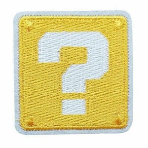 May include: Embroidered patch showing a yellow square with a white question mark. The patch has a white border and is designed for clothing or accessories. The design is inspired by a well-known video game.