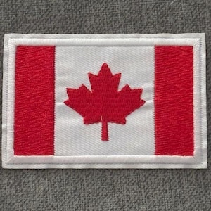 May include: A rectangular patch depicting the Canadian flag. The flag features a red maple leaf on a white background, with two red vertical bars. The patch is edged with white stitching.