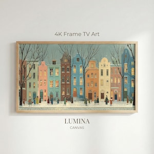 May include: A framed print depicting a winter scene of a European street with colorful buildings and figures. The artwork is labelled "4K Frame TV Art" and "LUMINA CANVAS". The buildings are painted in shades of pink, blue, orange, and yellow.