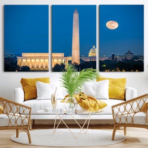 May include: A three-panel canvas print depicting Washington D.C. at dusk. The panels show the Lincoln Memorial, Washington Monument, Capitol Building, and a full moon against a deep blue sky. The artwork is displayed above a white sofa with yellow pillows.
