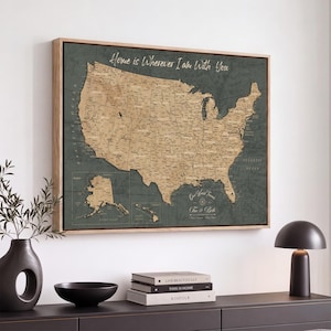 May include: A framed wall map of the United States in tan and dark green, featuring the text Home is Wherever I am With You, Our World Travels, and Tim & Beth. The map includes Alaska and Hawaii insets, state borders, and major cities.