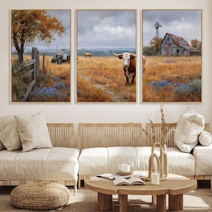 May include: A triptych of framed landscape paintings depicting a rural scene. The paintings feature a brown and white longhorn, a tractor, a barn, and a windmill in a field of brown grass and blue flowers under a cloudy sky.