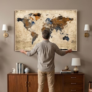 May include: A large framed world map with a vintage aesthetic. The map features a beige background with brown, blue, and orange accents. The map is being held by a person. The map is a decorative piece.