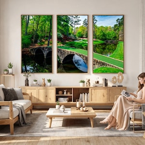 May include: Three framed landscape prints depicting golf course scenes with stone bridges over water. The prints feature lush green grass, trees, and reflections in the water. The frames are a warm wood tone, and the overall aesthetic is serene.