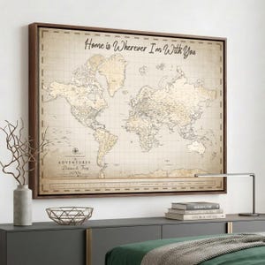 May include: A rectangular framed wall art piece featuring a vintage-style world map on a beige background. The text "Home is Wherever I'm With You" is printed at the top, with "The Adventures of Danna & Troy" and a compass rose visible below.