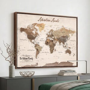May include: A framed world map wall art piece featuring a vintage-style aesthetic with sepia and brown tones. The text Adventure Awaits is printed at the top, and the text Our Adventures The Blincoe Family is printed in the lower left corner.