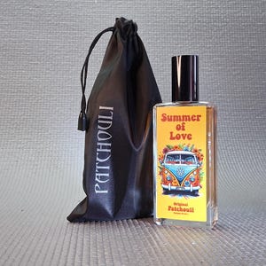 Op de afbeelding: Een heldere parfumfles met een zwarte dop en een geel etiket met de tekst "Summer of Love" en een VW-busje. Een zwart zakje met trekkoord met de tekst "PATCHOULI" staat naast de fles.