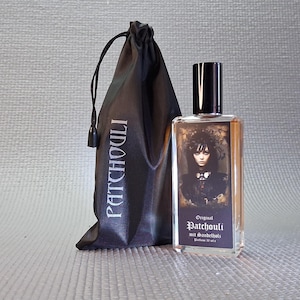 Puede incluir: Un frasco de perfume con tapón negro y una bolsa negra con cordón. El frasco tiene una etiqueta con un retrato de mujer y el texto "Original Patchouli". La bolsa tiene la palabra "Patchouli" impresa.