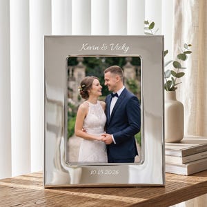May include: A rectangular silver-toned metal picture frame with a polished finish. The top border is engraved with the text Kevin & Vicky, and the bottom border is engraved with the date 10.15.2026. The frame holds a photograph of a couple.