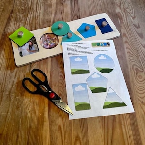 May include: A wooden puzzle with various geometric shapes and a photo frame. The puzzle pieces are in green, blue, and teal. A pair of black scissors with a red center is also present. A sheet of paper with shape cutouts is next to the puzzle.