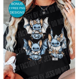May include: Black t-shirt featuring three blue bat illustrations holding jack-o'-lanterns. The bats have floral accents and patterned wings. The shirt also has the text "BONUS 2 FREE PNG DESIGNS".