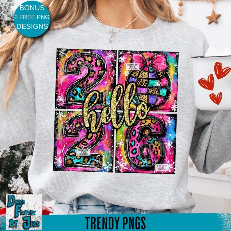May include: A light gray sweatshirt featuring a colorful graphic design. The design includes the numbers "26" with leopard print accents, the word "hello" in gold glitter, and a decorative ornament. The design is set against a vibrant, multi-colored background.